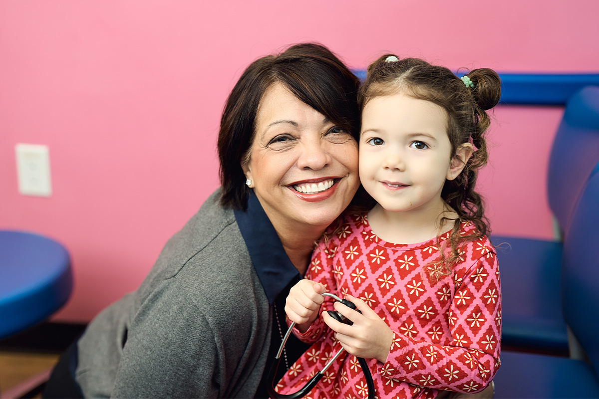 Dr. Sandra Peak of the Lewisville primary care office smiling with a little girl in pink