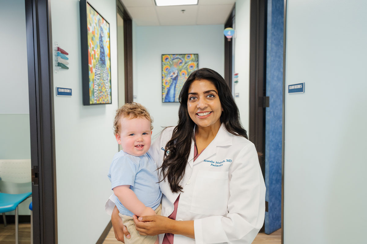 Pediatric physician smiling and holding a baby after a health check at a pediatric primary care office in Plano, Texas