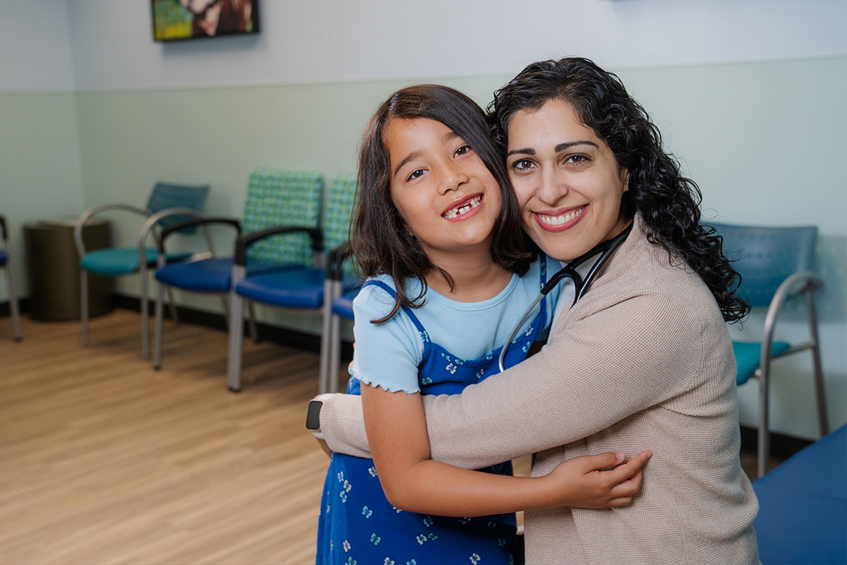 A pediatric physician hugging a patient after caring for the pediatric patient&rsquo;s health