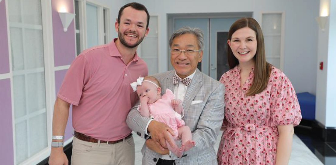 Doctor holding girl in pink flanked by parents