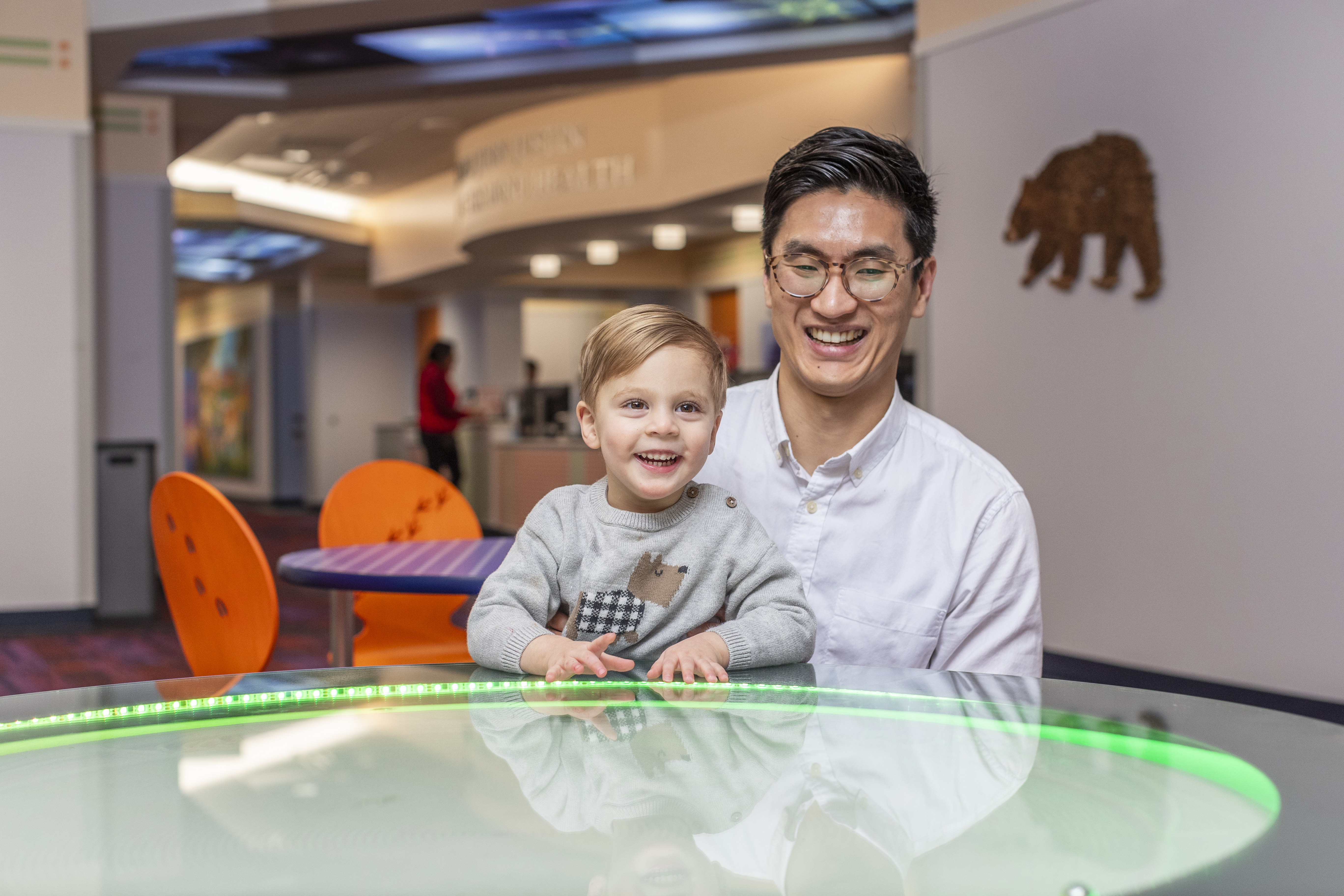 Young boy wearing a grey sweater with a dog on it sitting at a table with green lights
